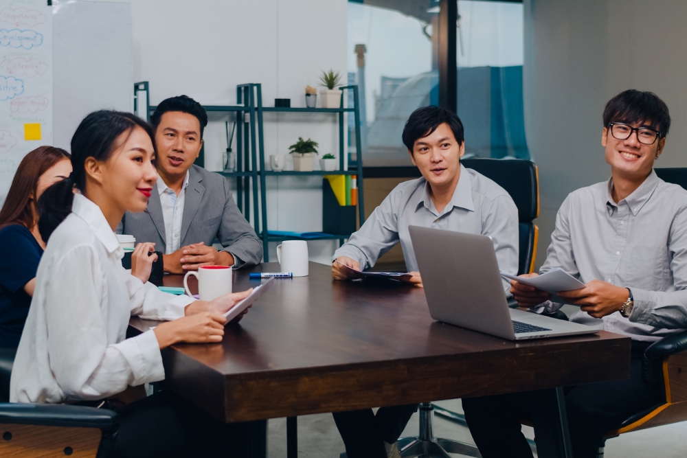 Millennial Asia businessmen and businesswomen having conference video call meeting brainstorming ideas about new project colleagues working together planning strategy enjoy teamwork in modern office.